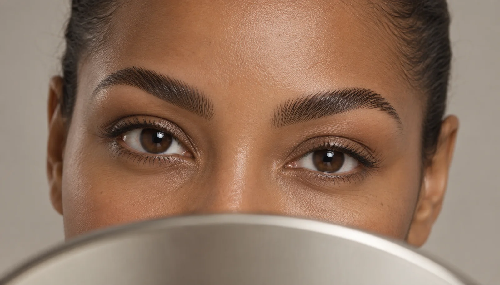 Close-up of softly laminated brows above a handheld mirror
